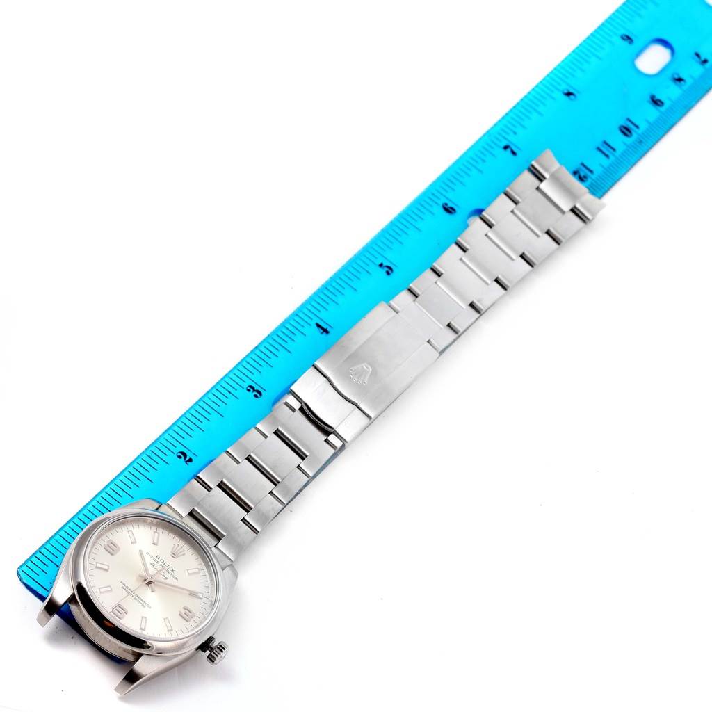 The Rolex Air-King 114200 Men's Stainless Steel Silver Dial 114200 Men's Stainless Steel Silver Dial watch is shown laid flat with its face and bracelet fully visible next to a blue ruler for scale.