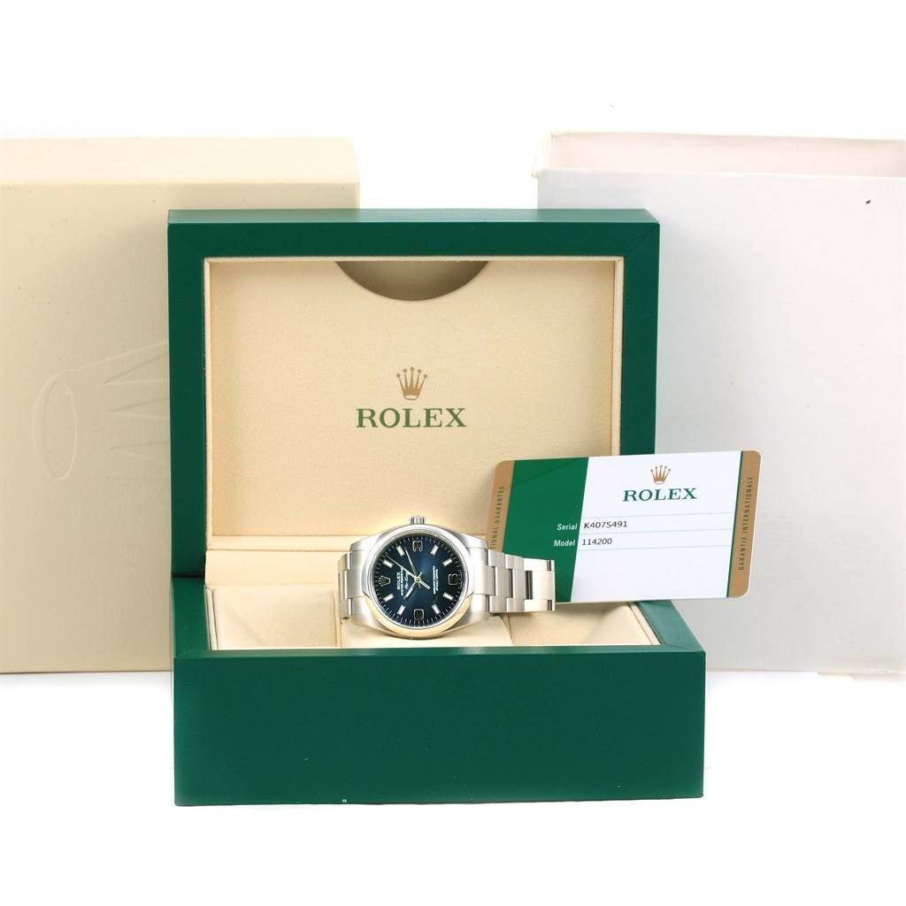 The image shows a Rolex Air-King 114200 Men's Stainless Steel Blue Dial 114200 Men's Stainless Steel Blue Dial watch placed in its green box with the certification card beside it.