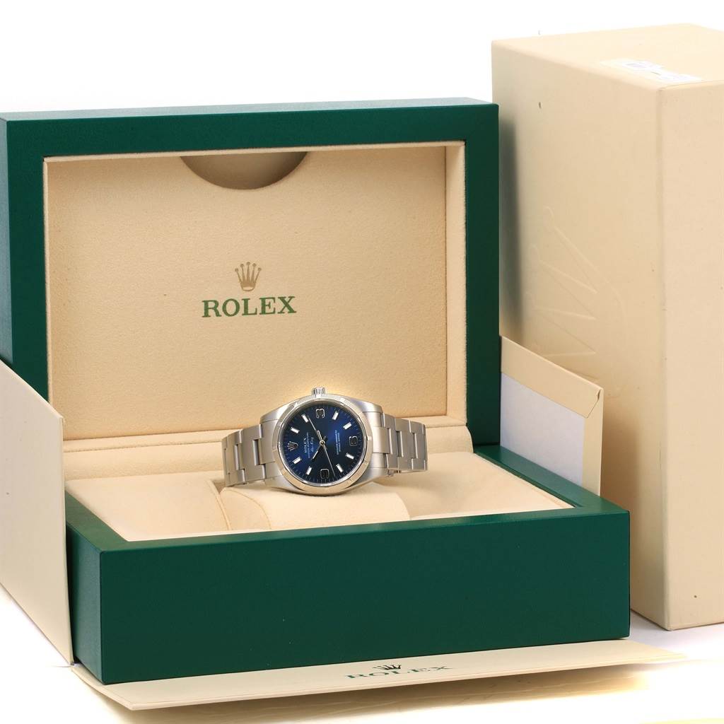 The Rolex Air-King 114210 Men's Stainless Steel Blue Dial 114210 Men's Stainless Steel Blue Dial watch is displayed head-on in its green and beige branded box with a stainless steel bracelet.