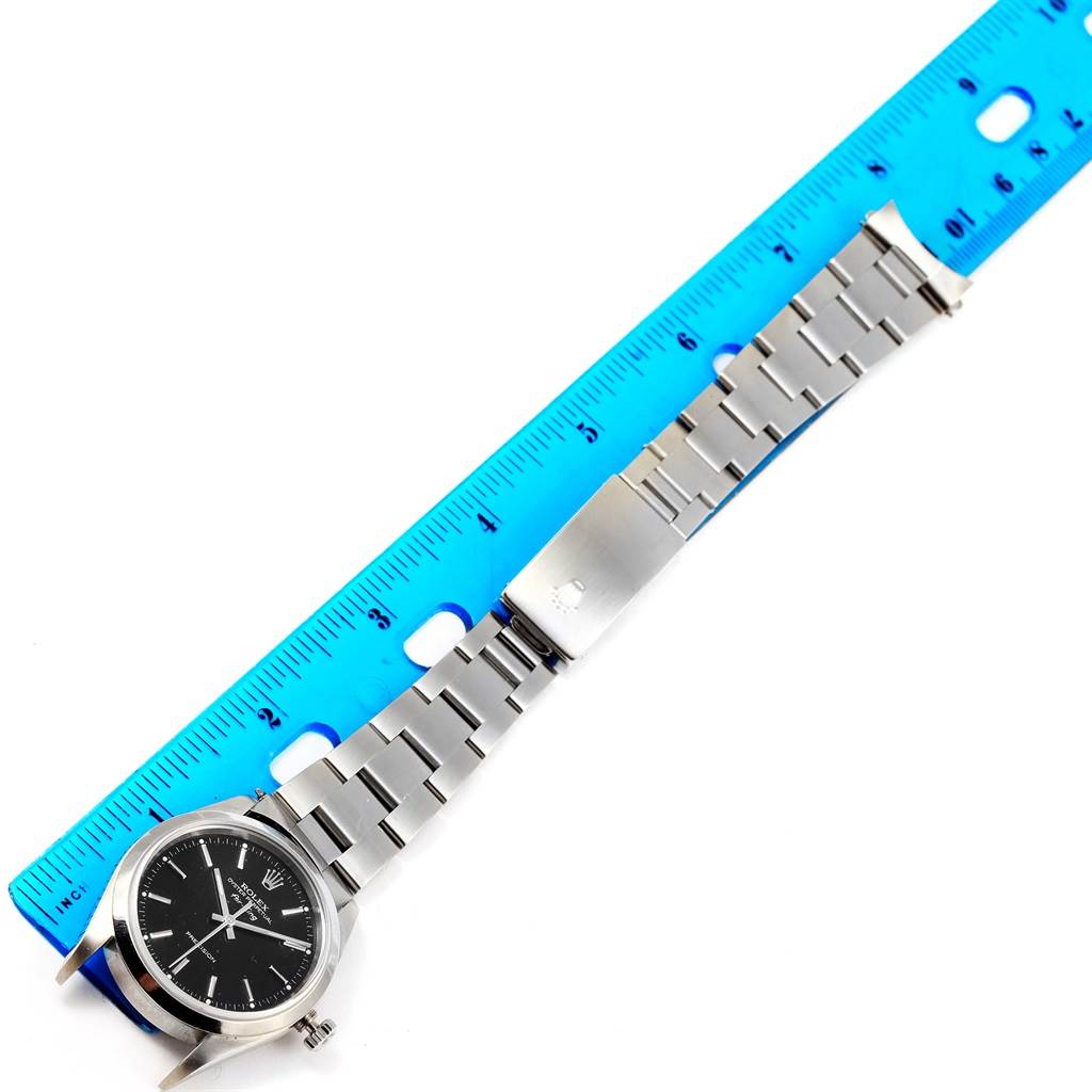 The image shows a flat-lay view of a Rolex Air-King 14000 Men's Stainless Steel Black Dial 14000 Men's Stainless Steel Black Dial watch beside a blue ruler, highlighting the watch's face, bracelet, and clasp.