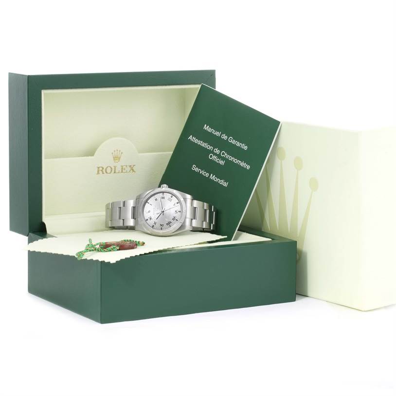 The Rolex Air-King 114210 Men's Stainless Steel Silver Dial 114210 Men's Stainless Steel Silver Dial watch is displayed in an open box next to its warranty manual.