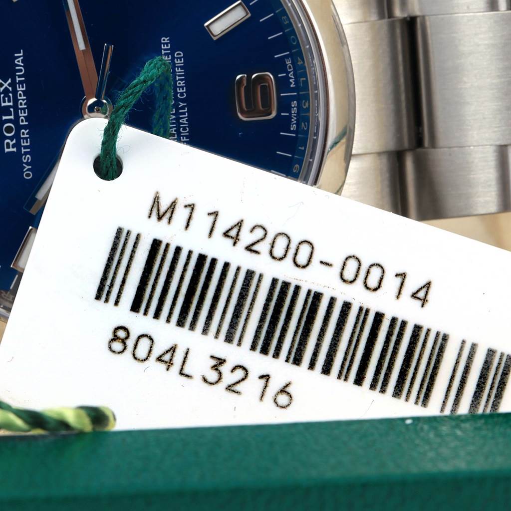 The image shows a close-up of a Rolex Air-King 114200 Men's Stainless Steel Blue Dial 114200 Men's Stainless Steel Blue Dial watch dial, part of the case, bracelet, and a tag with the model number.