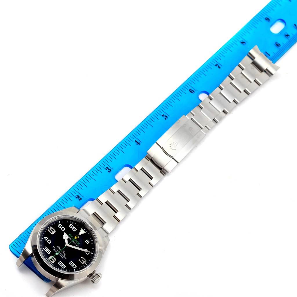 The image shows a top-down view of a Rolex Air-King 116900 Men's Stainless Steel Black Dial 116900 Men's Stainless Steel Black Dial watch, with the face, bracelet, and clasp visible next to a blue ruler.