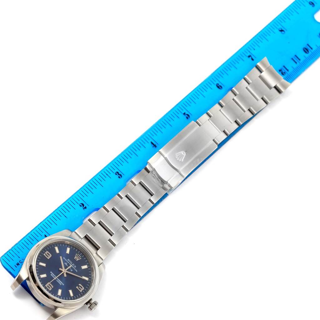 The image shows the Rolex Air-King 114200 Men's Stainless Steel Blue Dial 114200 Men's Stainless Steel Blue Dial watch laid flat with its bracelet extended next to a blue ruler.