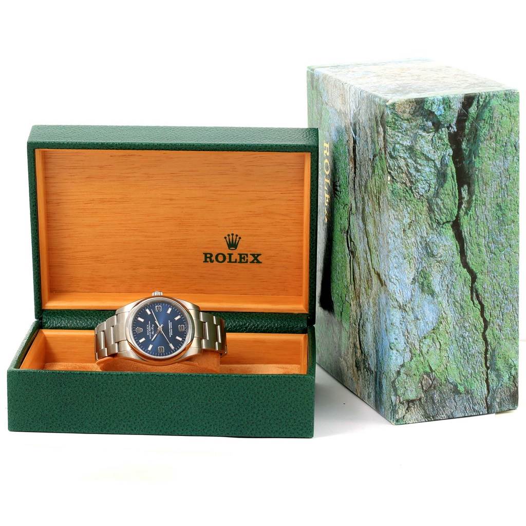 The Rolex Air-King 114200 Men's Stainless Steel Blue Dial 114200 Men's Stainless Steel Blue Dial watch is displayed on a stand inside an open, branded green and wood box, with the outer textured box visible beside it.