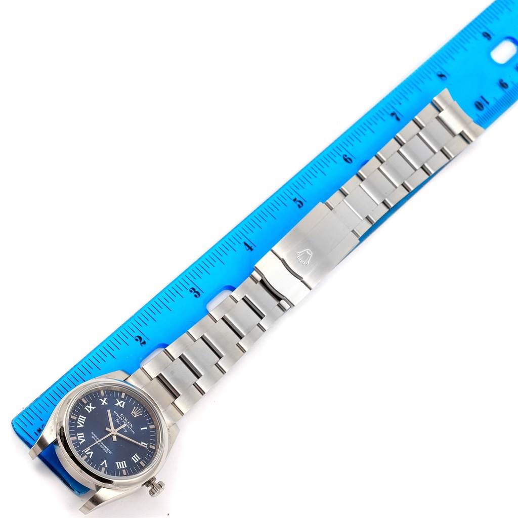 The image shows a top view of a Rolex Air-King 114200 Men's Stainless Steel Blue Dial 114200 Men's Stainless Steel Blue Dial watch with a silver bracelet next to a blue ruler.