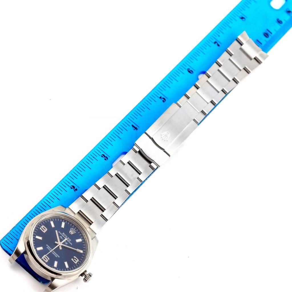This image shows a Rolex Air-King 114200 Men's Stainless Steel Blue Dial 114200 Men's Stainless Steel Blue Dial watch with a blue dial and metal bracelet, positioned next to a blue ruler for scale.