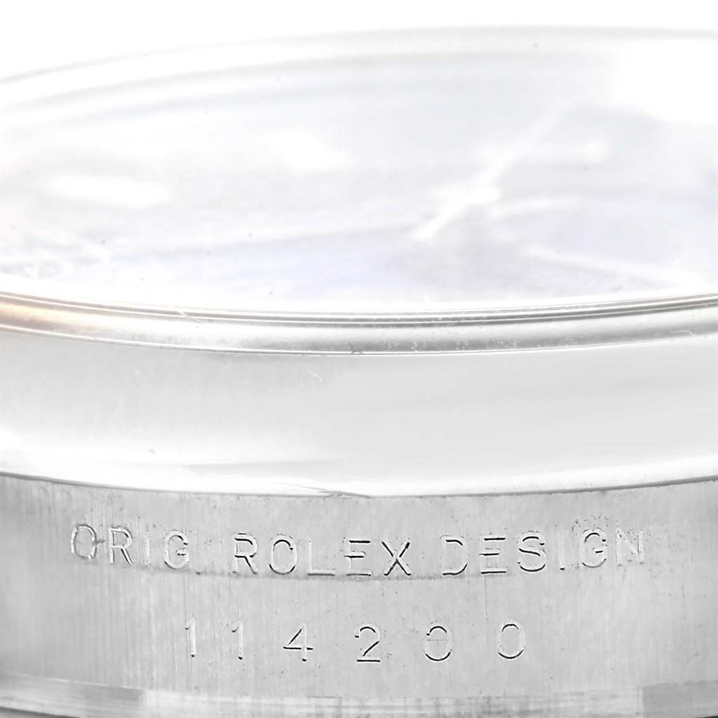 The image shows a close-up of the side of the Rolex Air-King 114200 Men's Stainless Steel Blue Dial 114200 Men's Stainless Steel Blue Dial watch, featuring the engraving "ORIG. ROLEX DESIGN" and the model number "114200."