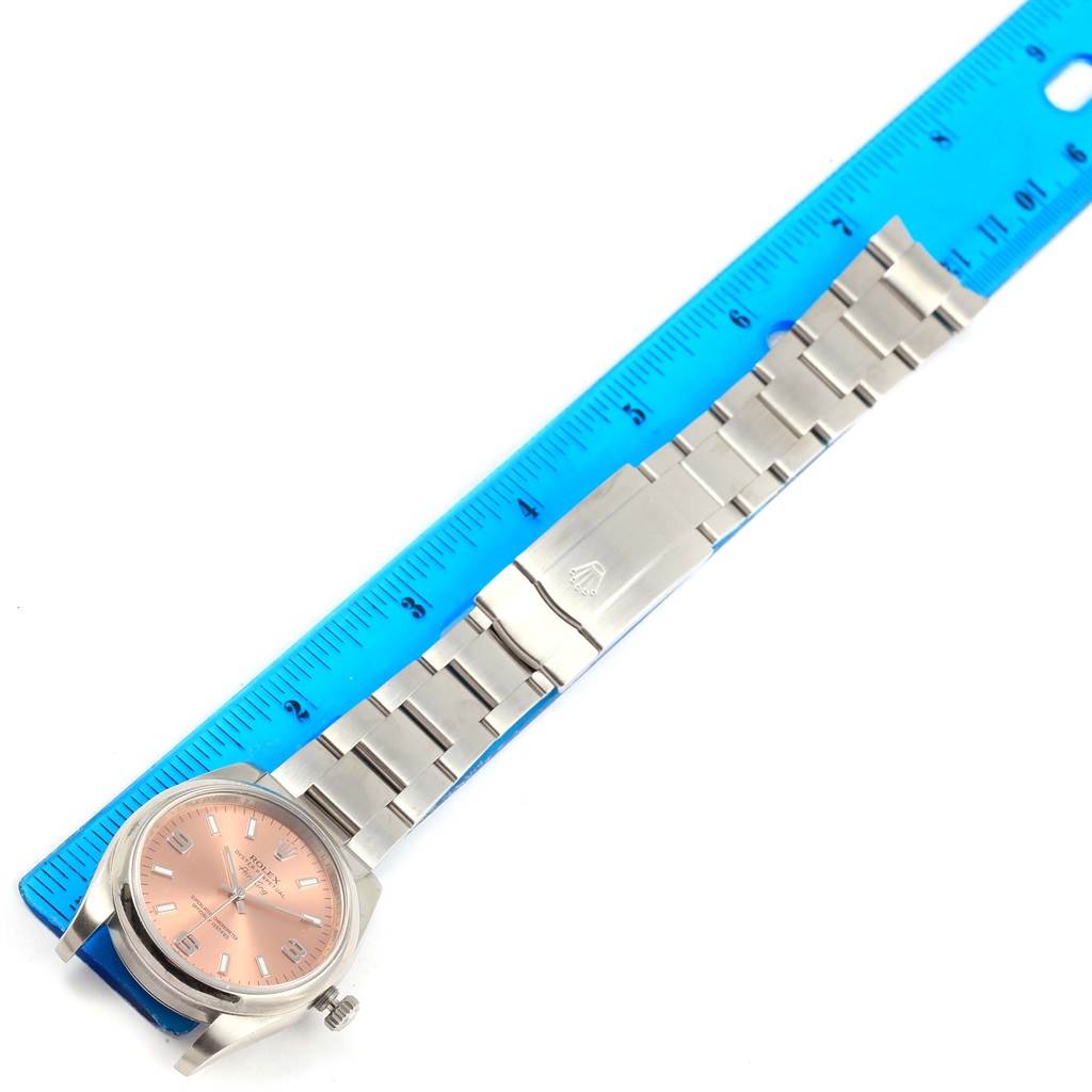 The image shows a top view of a Rolex Air-King 114200 Men's Stainless Steel Pink Dial 114200 Men's Stainless Steel Pink Dial watch with a pink dial, next to a blue ruler for size reference.