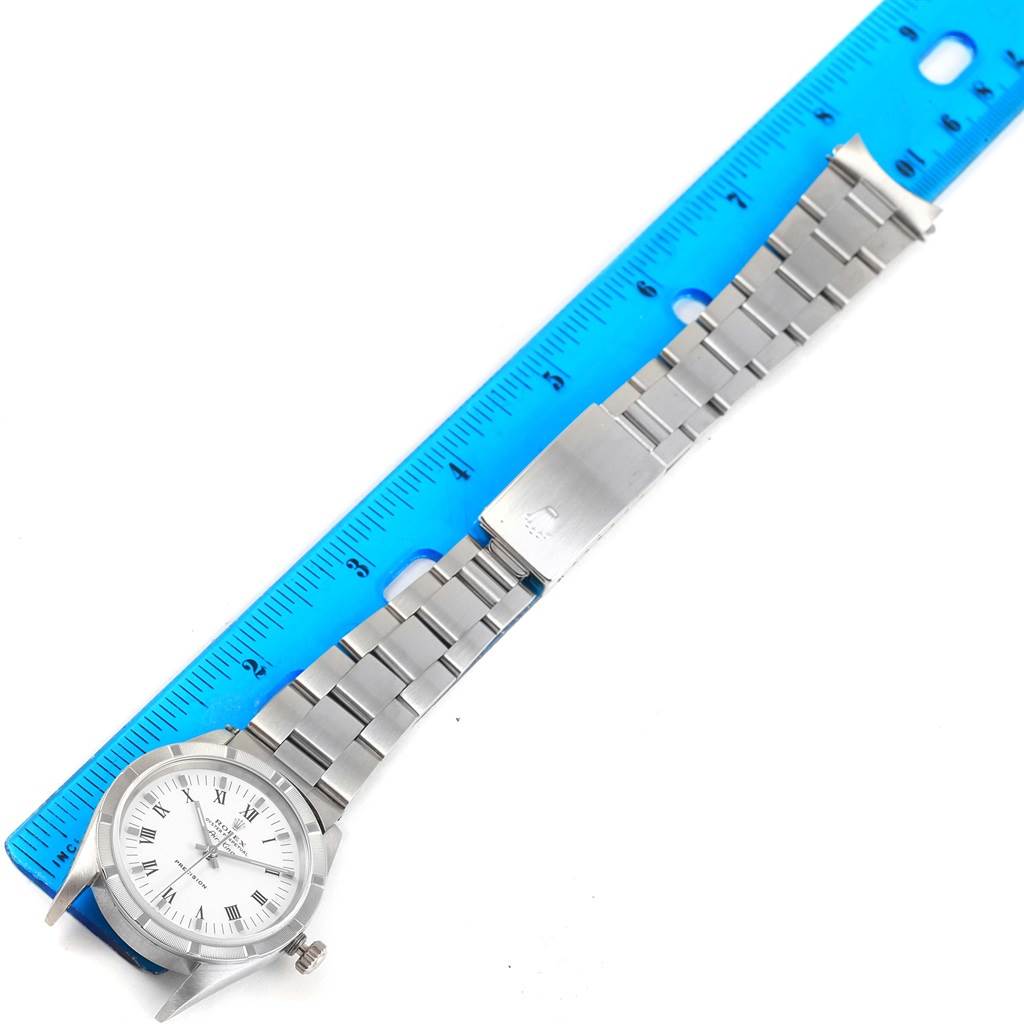 The image shows a top-down view of a Rolex Air-King 14010 Men's Stainless Steel White Dial 14010 Men's Stainless Steel White Dial watch, including its face, bracelet, and clasp, positioned next to a blue ruler.