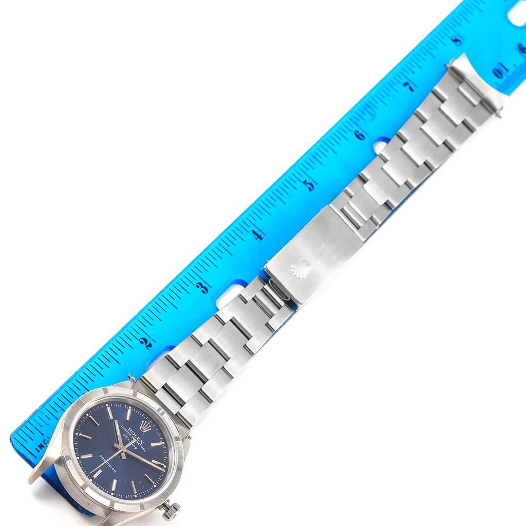 The Rolex Air-King 14010 Men's Stainless Steel Blue Dial 14010 Men's Stainless Steel Blue Dial watch is shown laying flat with its stainless steel bracelet extended alongside a blue ruler for measurement.