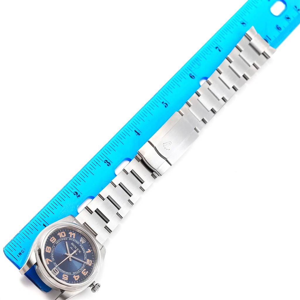 The image shows a Rolex Air-King 114200 Stainless Steel Blue Dial 114200 Stainless Steel Blue Dial watch and its stainless steel band measured against a blue ruler, displayed flat and fully extended.