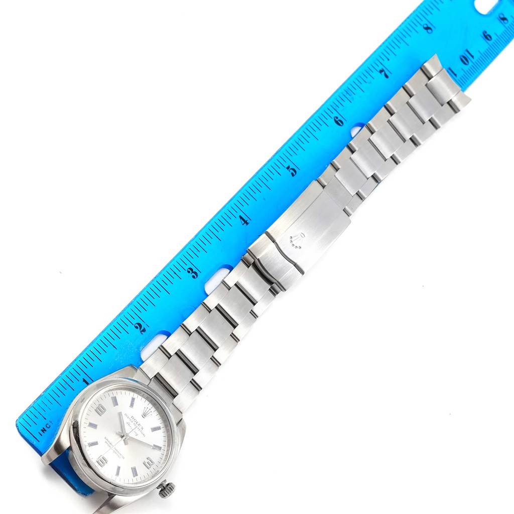 The image shows a top-down view of a Rolex Air-King 114200 Men's Stainless Steel Silver Dial 114200 Men's Stainless Steel Silver Dial watch placed along a ruler, highlighting the watch face, band, and clasp.