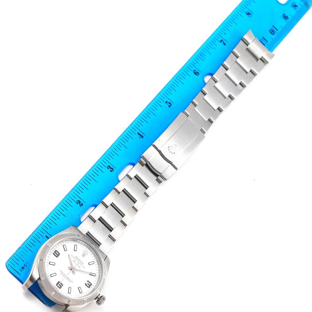 The image shows a top-down view of a Rolex Air-King 114210 Men's Stainless Steel White Dial 114210 Men's Stainless Steel White Dial watch with its bracelet laid beside a blue ruler for measurement.