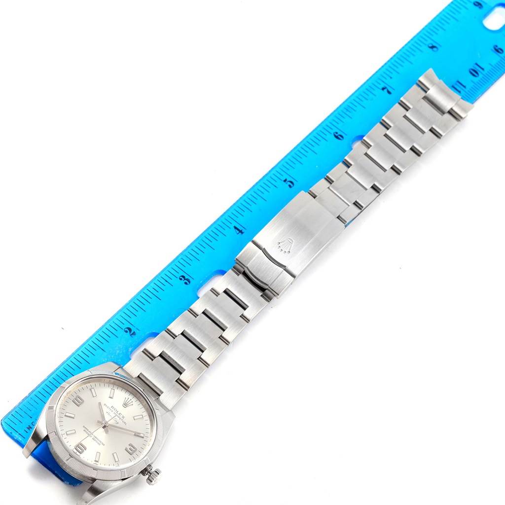 This is a top-down view of a Rolex Air-King 114210 Stainless Steel Silver Dial 114210 Stainless Steel Silver Dial watch next to a blue ruler, showing its face, bracelet, and clasp.