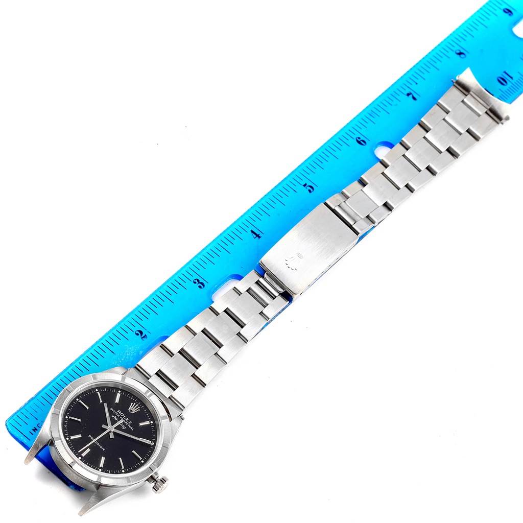 The Rolex Air-King 14010 Men's Stainless Steel Black Dial 14010 Men's Stainless Steel Black Dial watch is shown from a top-down angle, featuring its face and metal bracelet, next to a blue ruler.