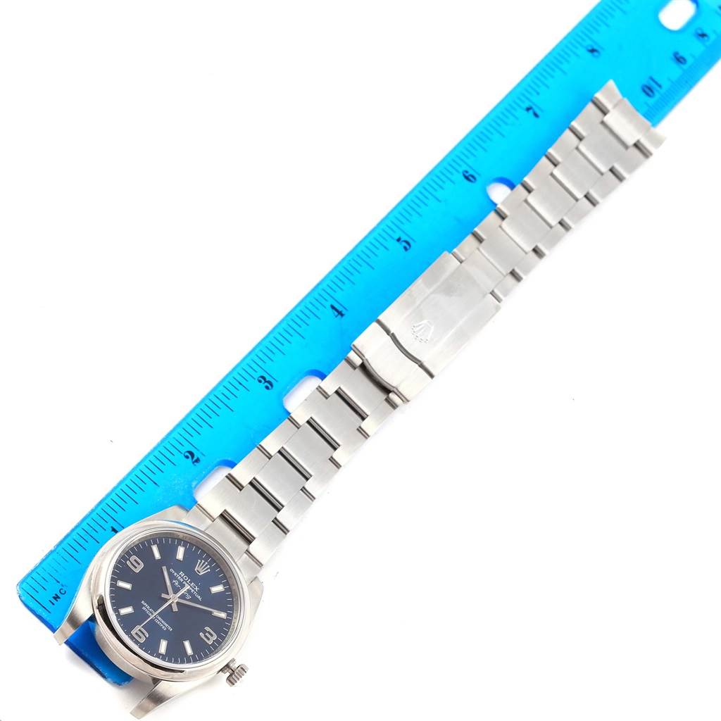 The image shows a Rolex Air-King 114200 Men's Stainless Steel Blue Dial 114200 Men's Stainless Steel Blue Dial watch lying flat with its full stainless steel bracelet extended alongside a blue ruler.