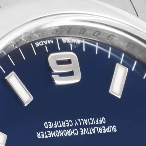 Close-up of the dial of a Rolex Air-King 114200 Men's Stainless Steel Blue Dial 114200 Men's Stainless Steel Blue Dial watch showing the 9 o'clock marker, part of the bezel, and text indicating certification.