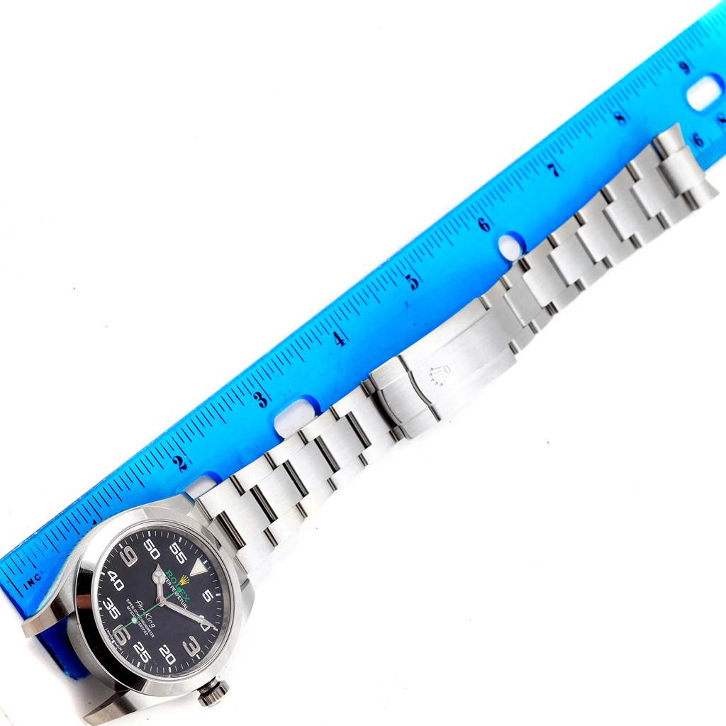 The Rolex Air-King 116900 Men's Stainless Steel Black Dial 116900 Men's Stainless Steel Black Dial watch is shown from an overhead angle, displaying the face, bracelet, and clasp alongside a blue ruler for scale.