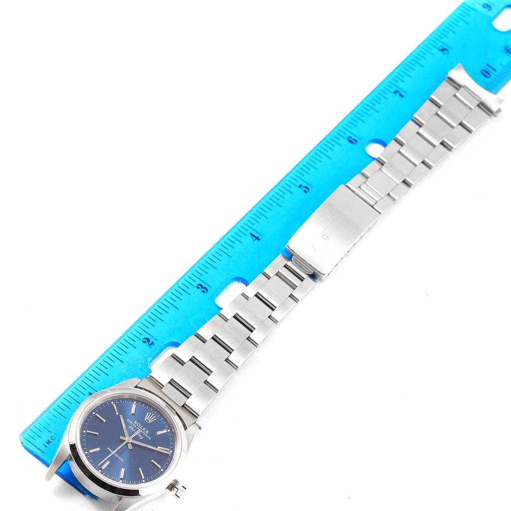 The image shows the full length of a Rolex Air-King 14000 Men's Stainless Steel Blue Dial 14000 Men's Stainless Steel Blue Dial watch, featuring its stainless steel bracelet and face, against a blue ruler.