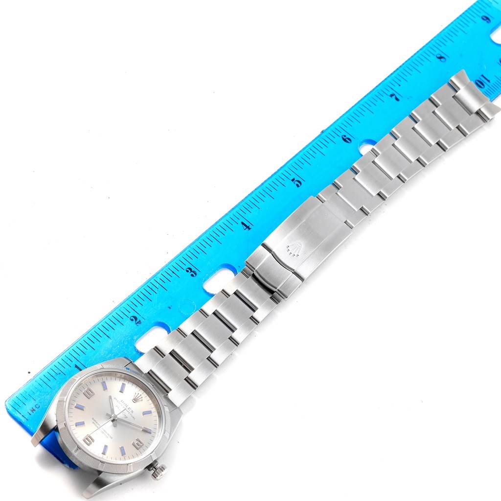 The image shows an aerial view of a Rolex Air-King 114210 Men's Stainless Steel Silver Dial 114210 Men's Stainless Steel Silver Dial watch alongside a blue ruler for scale.