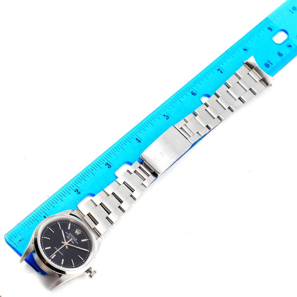 The image shows an overhead view of a Rolex Air-King 14000 Men's Stainless Steel Black Dial 14000 Men's Stainless Steel Black Dial watch with its bracelet and clasp laid next to a blue ruler.