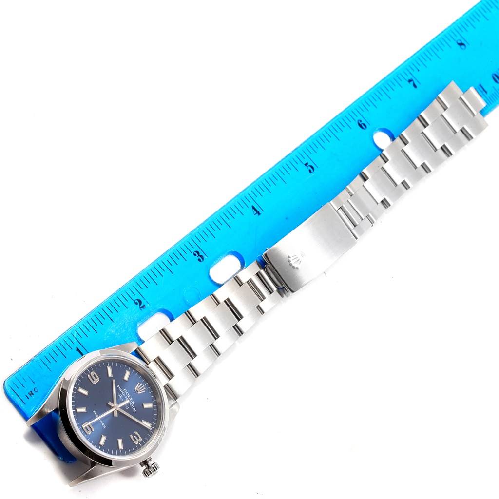 The image shows a Rolex Air-King 14000 Men's Stainless Steel Blue Dial 14000 Men's Stainless Steel Blue Dial watch with a blue dial and stainless steel bracelet next to a blue ruler.