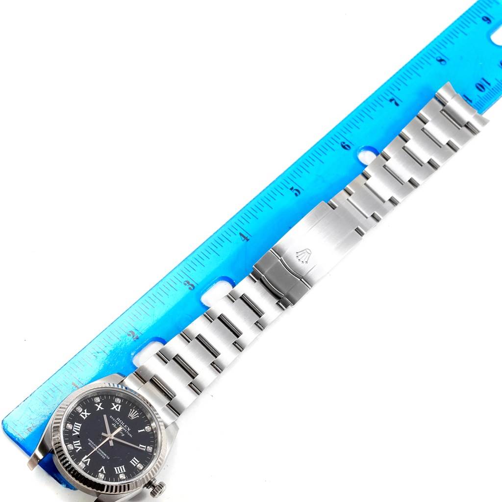 The image shows a top-down view of a Rolex Air-King 114234 Men's Stainless Steel Black Dial 114234 Men's Stainless Steel Black Dial watch, highlighting the face, bezel, and bracelet alongside a blue ruler.