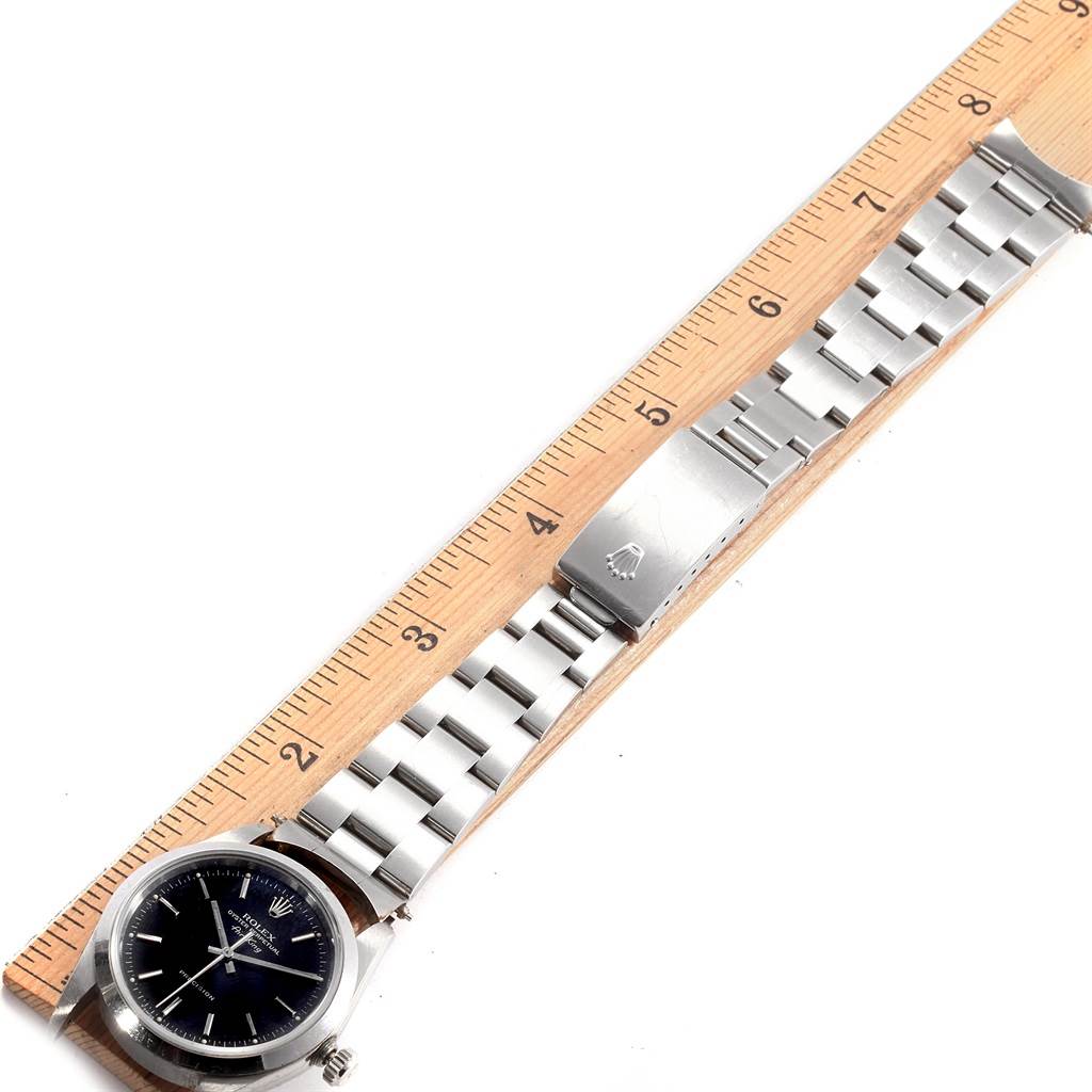 The Rolex Air-King 14000 Men's Stainless Steel Black Dial 14000 Men's Stainless Steel Black Dial watch is displayed face-up with its metal band extended along a wooden ruler.