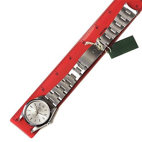 The Rolex Air-King 1400 Men's Stainless Steel Silver Dial 1400 Men's Stainless Steel Silver Dial watch is shown from a top-down angle, displaying the face, bracelet, and attached tags, placed against a red ruler.