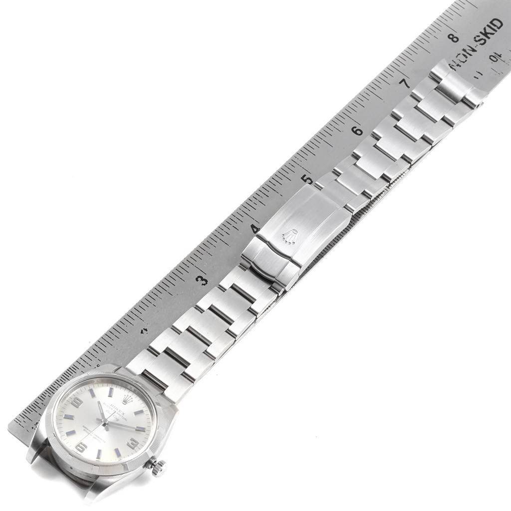 The Rolex Air-King 114210 Men's Stainless Steel Silver Dial 114210 Men's Stainless Steel Silver Dial watch is shown from an angled side view, displaying the watch face, band, and clasp next to a ruler for size reference.