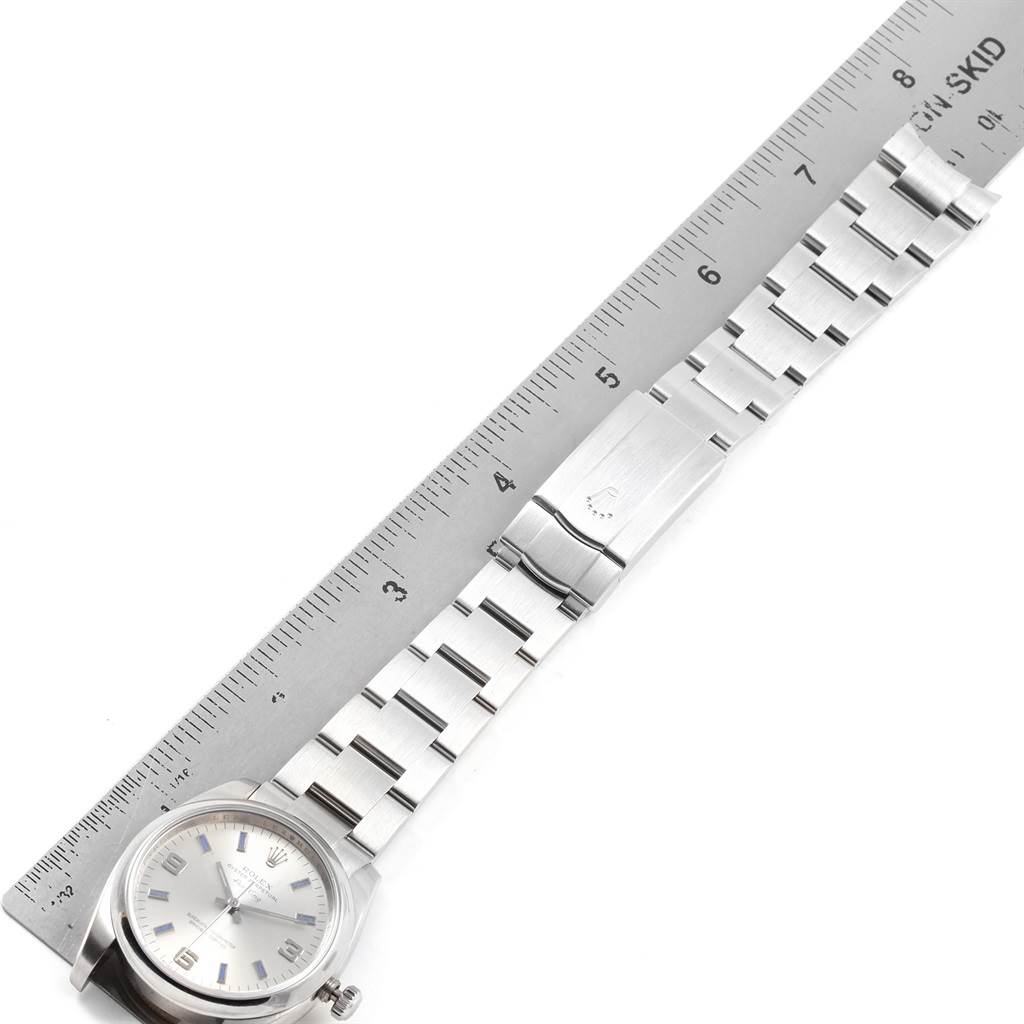 This image shows a top-down view of a Rolex Air-King 114200 Men's Stainless Steel Silver Dial 114200 Men's Stainless Steel Silver Dial watch, with the face and the full length of the metal bracelet next to a ruler. 