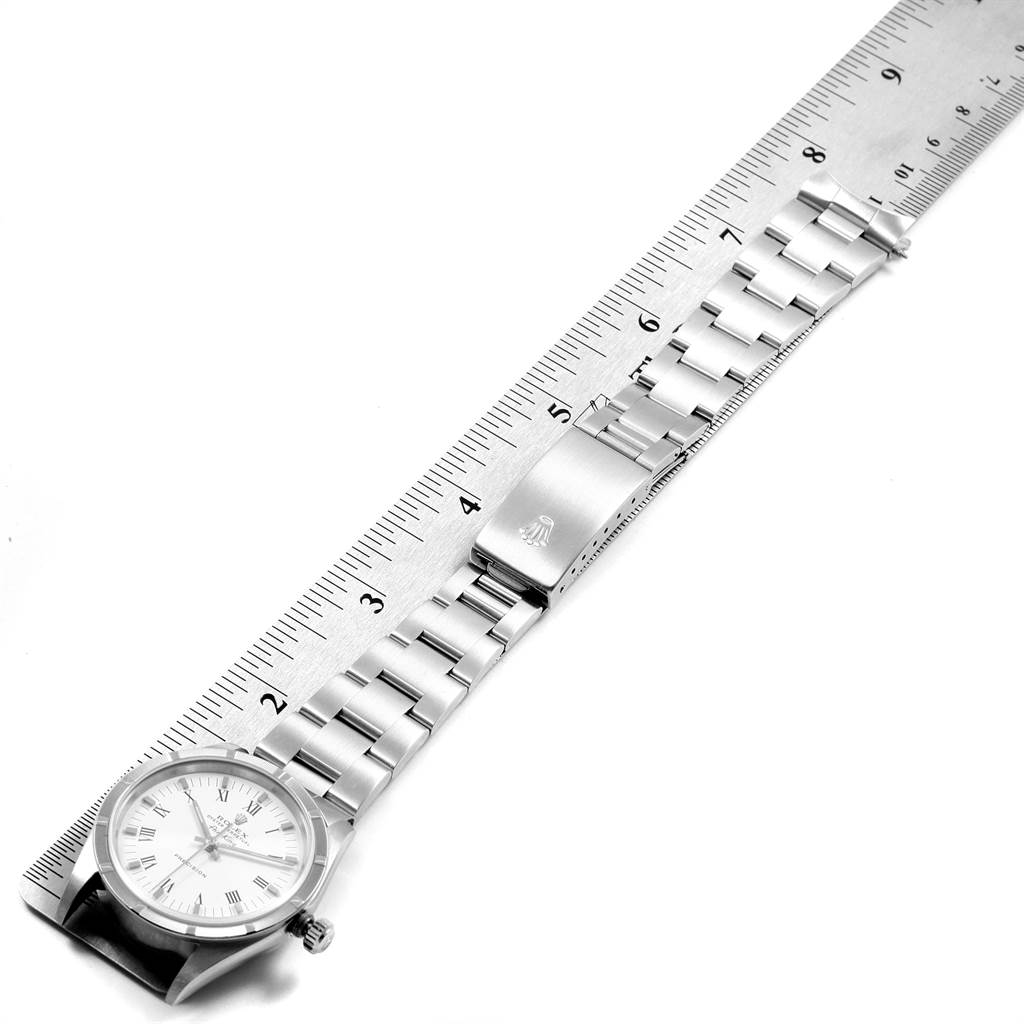 The Rolex Air-King 14010 Men's Stainless Steel White Dial 14010 Men's Stainless Steel White Dial watch is laid flat, displaying its dial, bracelet, and clasp next to a ruler for scale.