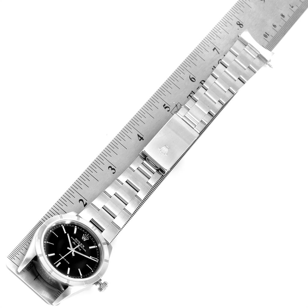 The Rolex Air-King 14010 Men's Stainless Steel Black Dial 14010 Men's Stainless Steel Black Dial watch is shown from a top-down angle, displaying the watch face, bracelet, and clasp resting on a ruler.