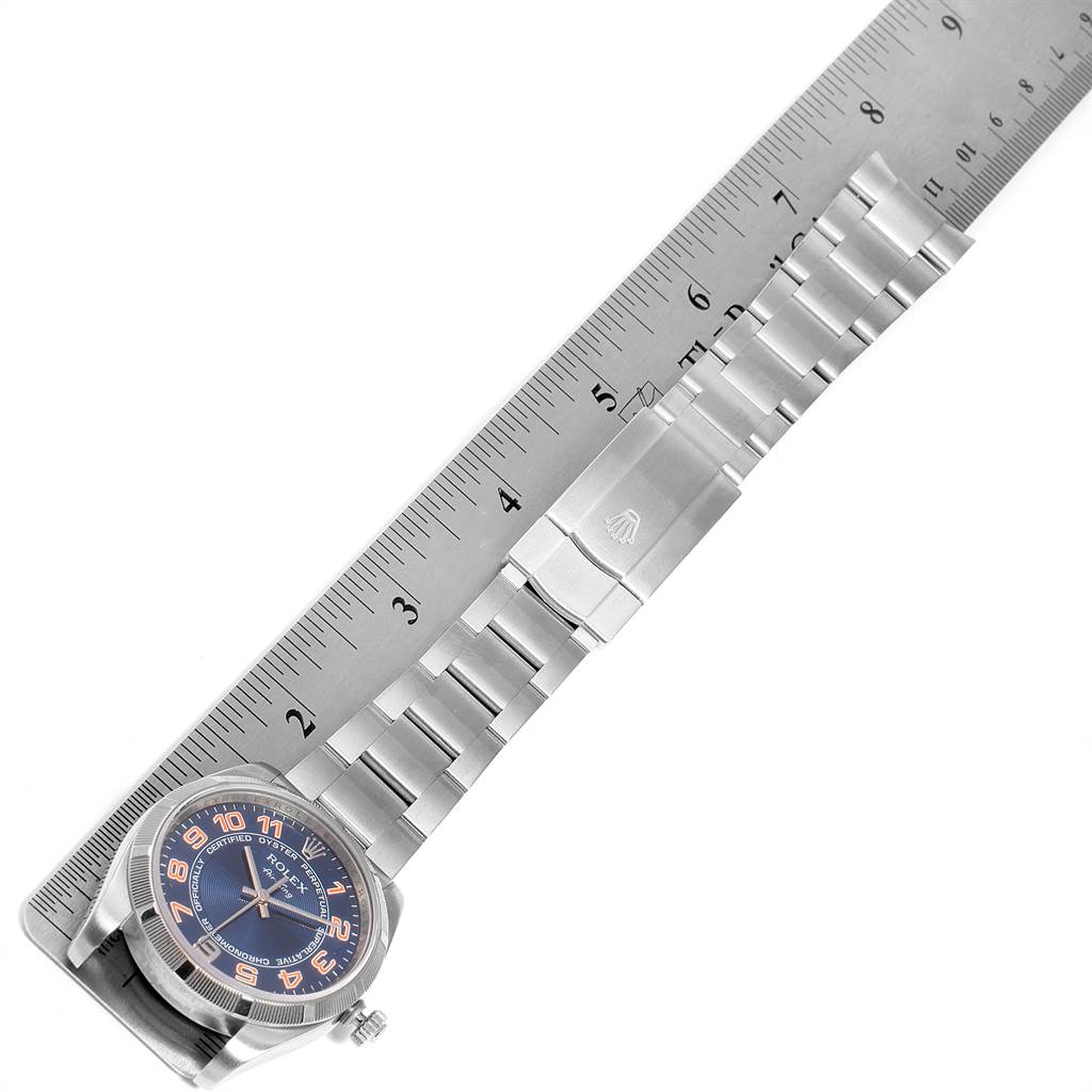 The Rolex Air-King 114210 Men's Stainless Steel Blue Dial 114210 Men's Stainless Steel Blue Dial watch is shown from a top-down angle with its entire bracelet and case visible, alongside a measuring ruler.