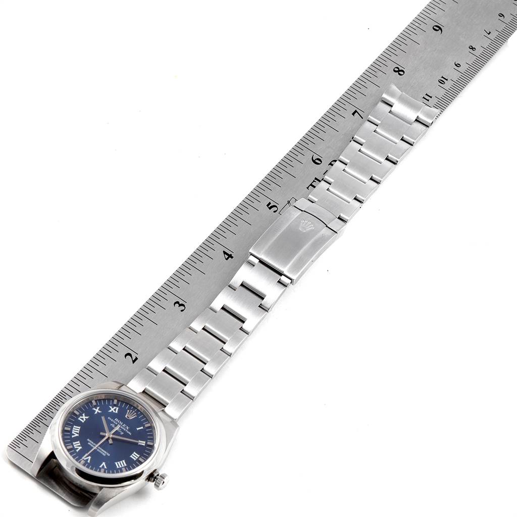 The image shows a Rolex Air-King 114200 Men's Stainless Steel Blue Dial 114200 Men's Stainless Steel Blue Dial watch placed perpendicular to a ruler, highlighting its metal band and partially its face.