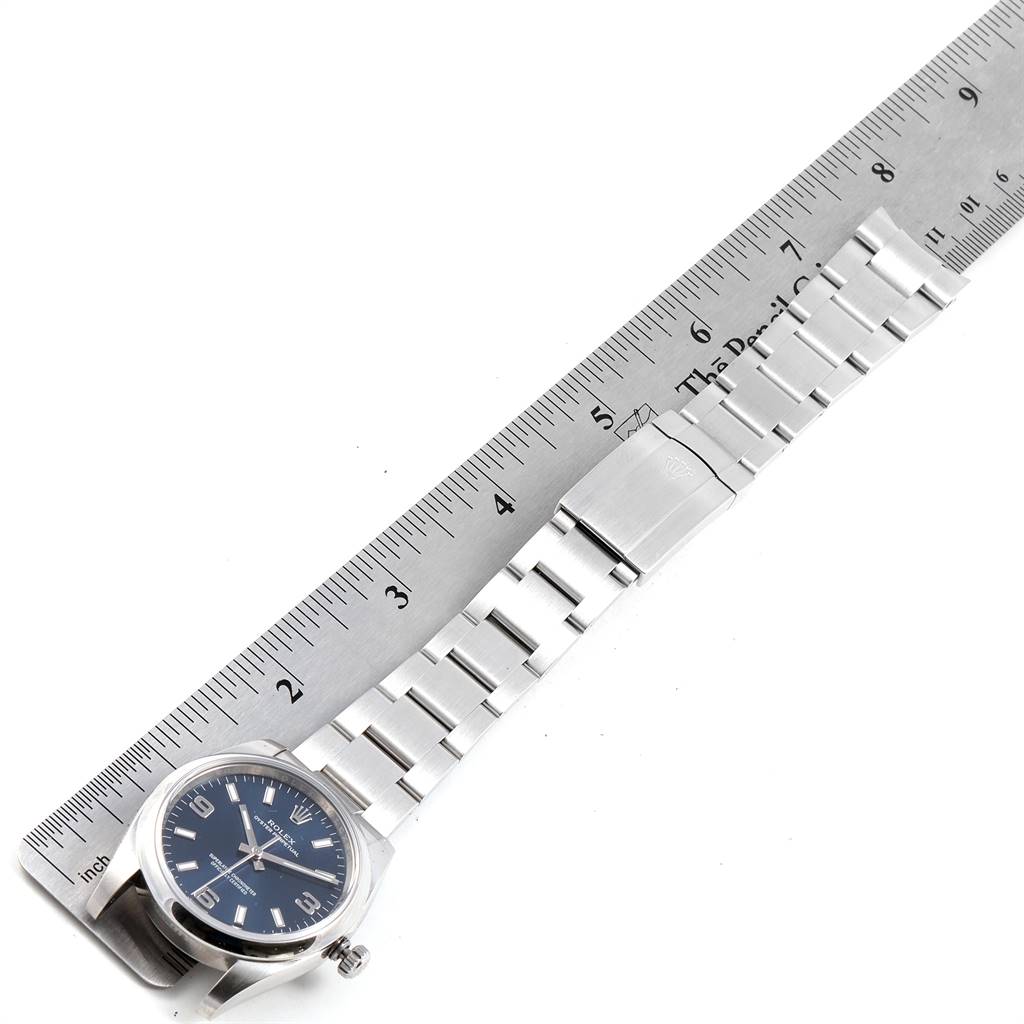 The image shows the front view of a Rolex Air-King 114200 Men's Stainless Steel Blue Dial 114200 Men's Stainless Steel Blue Dial watch, displaying the face and bracelet alongside a metal ruler.