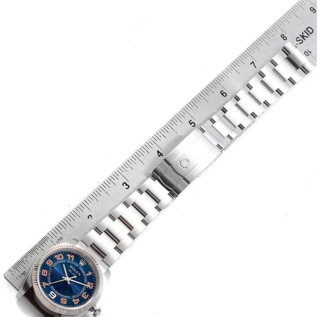 The image shows the Rolex Air-King 114234 Men
s Stainless Steel Blue Dial 114234 Men
s Stainless Steel Blue Dial watch from an overhead angle with its blue dial and metal bracelet alongside a ruler.