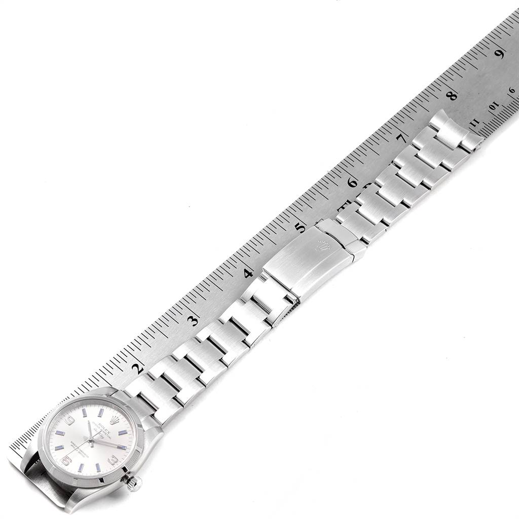 The Rolex Air-King 114210 Men's Stainless Steel Silver Dial 114210 Men's Stainless Steel Silver Dial watch is shown from an overhead angle, displaying the watch face and entire bracelet alongside a measuring ruler.