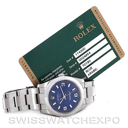 The image shows a Rolex Air-King 114200 Men's Stainless Steel Blue Dial 114200 Men's Stainless Steel Blue Dial watch laid flat with its certification card angled behind it.