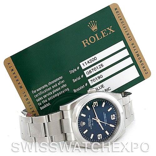 The image shows a Rolex Air-King 114200 Men's Stainless Steel Blue Dial 114200 Men's Stainless Steel Blue Dial watch laid flat, with a green Rolex certification card positioned behind it.