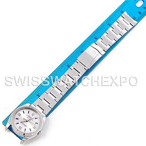 The Rolex Air-King 114210 Men's Stainless Steel Silver Dial 114210 Men's Stainless Steel Silver Dial watch is shown from a top-down angle, displaying its face, stainless steel bracelet, and clasp alongside a blue ruler.