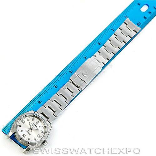 The image shows a top-down view of a Rolex Air-King 114210 Men's Stainless Steel Silver Dial 114210 Men's Stainless Steel Silver Dial watch alongside a blue ruler, highlighting its full metal bracelet.