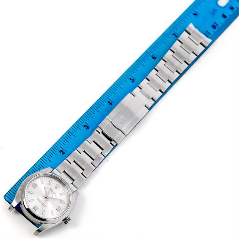 The Rolex Air-King 114200 Men's Stainless Steel Silver Dial 114200 Men's Stainless Steel Silver Dial watch is shown from an overhead angle, displaying the face and entire metal bracelet against a ruler.