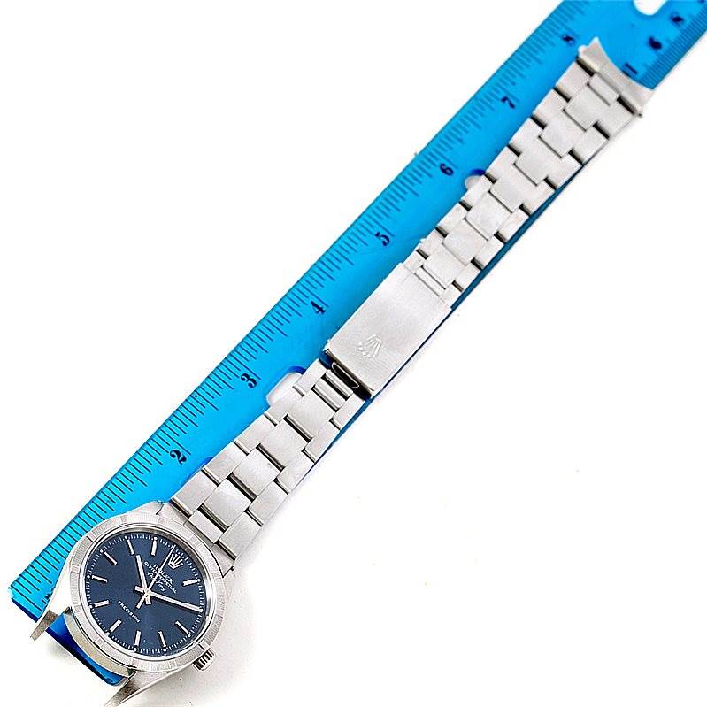 The image shows a Rolex Air-King 14010 Men's Stainless Steel Blue Dial 14010 Men's Stainless Steel Blue Dial watch laid flat along a blue ruler, displaying its face, bracelet, and clasp.