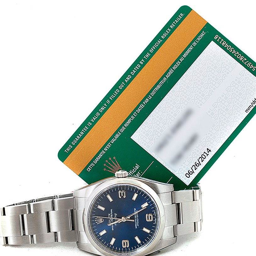 The image shows the Rolex Air-King 114200 Men's Stainless Steel Blue Dial 114200 Men's Stainless Steel Blue Dial watch at a slight angle, highlighting its face, bracelet, and a warranty card.
