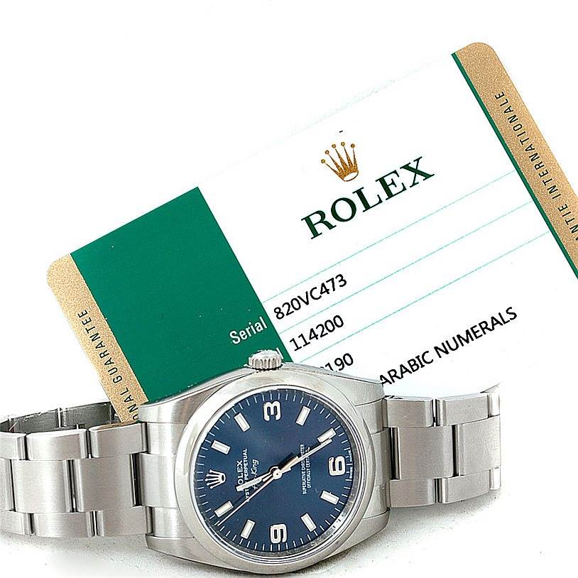 The image shows a Rolex Air-King 114200 Men's Stainless Steel Blue Dial 114200 Men's Stainless Steel Blue Dial watch lying flat, displaying its face and bracelet, alongside its certification card.