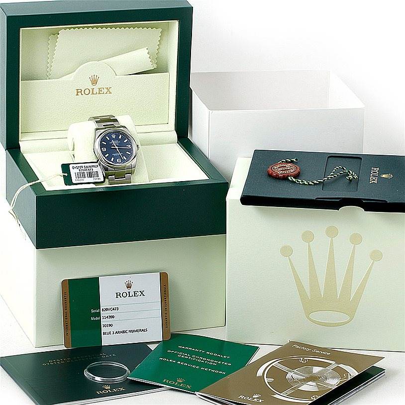 The image shows a Rolex Air-King 114200 Men's Stainless Steel Blue Dial 114200 Men's Stainless Steel Blue Dial watch displayed in its box, accompanied by accessories including booklets, a warranty card, and a tag.