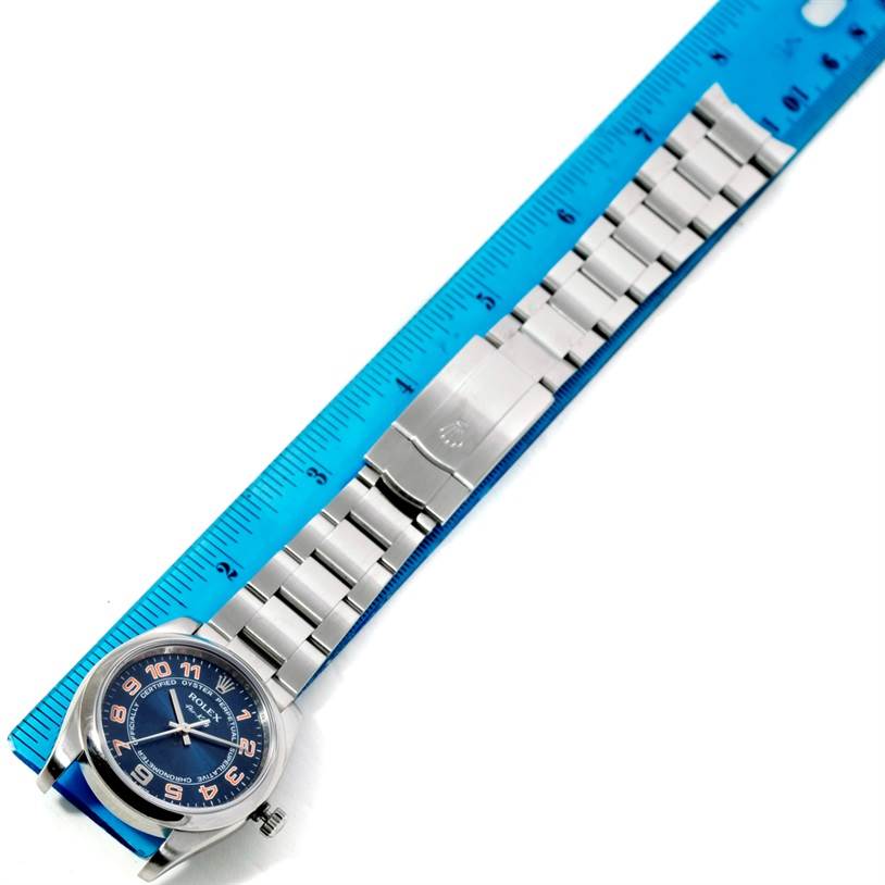The Rolex Air-King 114200 Men's Stainless Steel Blue Dial 114200 Men's Stainless Steel Blue Dial watch is shown lying flat with the face and bracelet visible, placed next to a blue ruler for measurement.