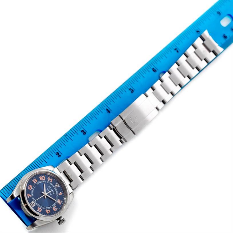 The image shows a top-down view of a Rolex Air-King 114200 Men's Stainless Steel Blue Dial 114200 Men's Stainless Steel Blue Dial watch, including the face, bracelet, and clasp, placed next to a blue ruler.